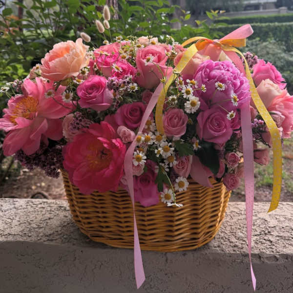 Pink and peach flowers arranged in a wicker basket with ribbon.