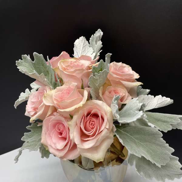 Pink roses arranged in a clear glass vase with silver foliage
