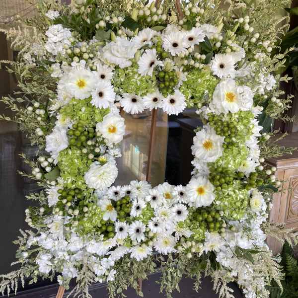 White floral wreath on a wooden easel with green accents