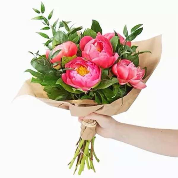 Handheld bouquet of pink peonies wrapped in brown paper