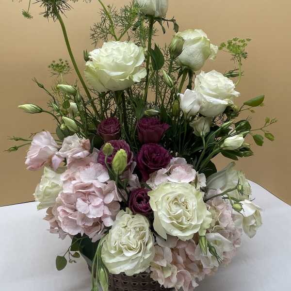 Tall floral arrangement with white roses, pink hydrangeas, and purple blooms in a basket