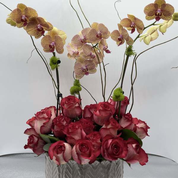Pink roses and yellow orchids arranged in a white ceramic vase