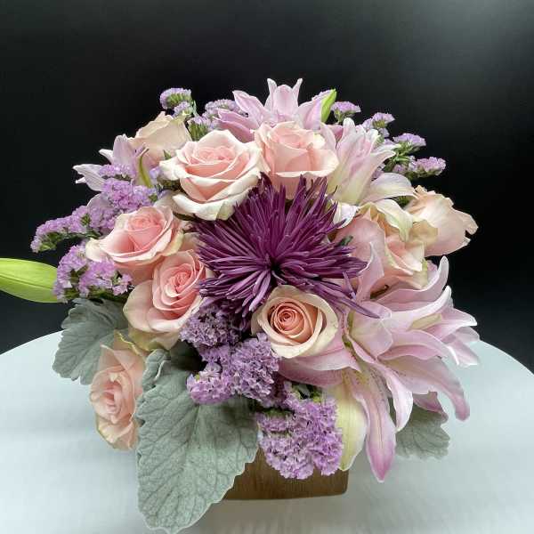 Pink roses and lilies arranged with purple blooms in a low vase