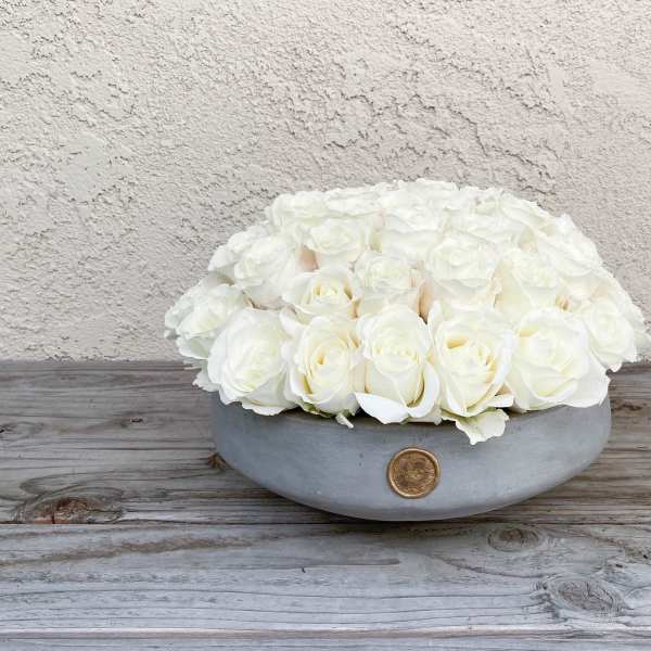 White roses arranged in a low gray bowl with a gold accent