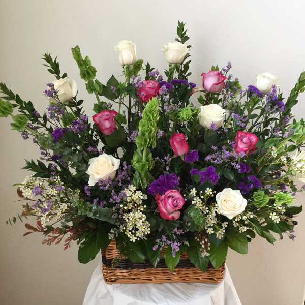 Basket arrangement of pink and white roses with purple filler flowers