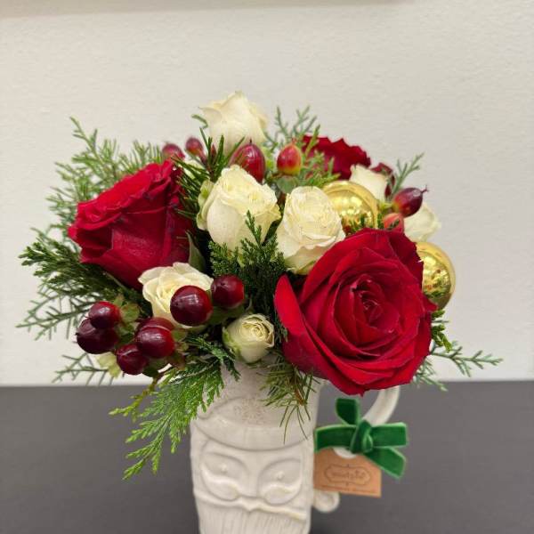 Compact arrangement of red and white roses with berries and evergreens in a white Santa mug.