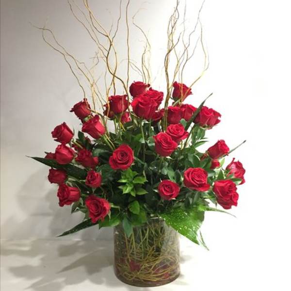 Red roses arranged in a clear glass vase with tall curly branches