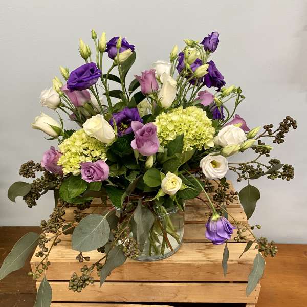 Purple and white flowers in a glass vase with trailing greenery
