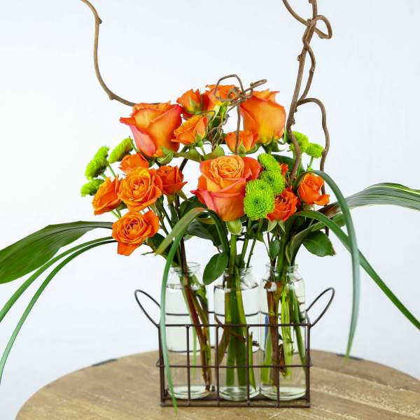 Orange roses in glass bottles with curly branches and green accents