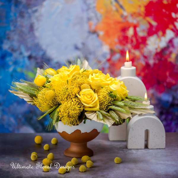 Yellow floral arrangement in a pedestal vase beside lit candles