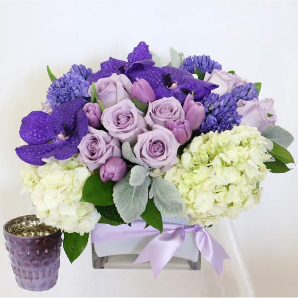 Lavender roses and purple orchids arranged with hydrangeas in a square vase