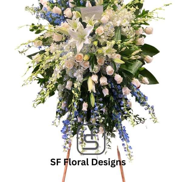 Tall standing spray of white lilies, cream roses, and blue delphinium on a wooden easel