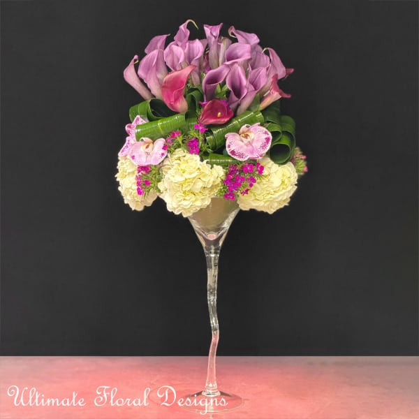 Pink and purple floral arrangement in a tall glass stemware vase