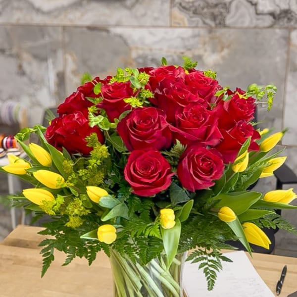 Red roses and yellow tulips arranged in a clear glass vase
