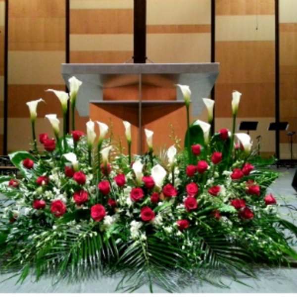 Large altar arrangement of red roses and white calla lilies in front of a church pulpit