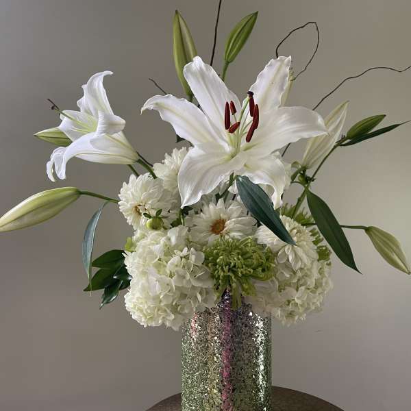White lilies and white blooms arranged in a tall silver vase