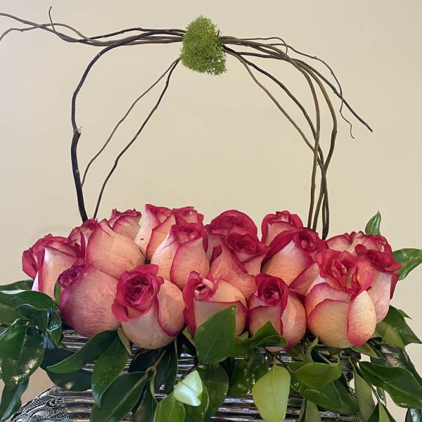 Pink roses arranged in a basket with curly branches arching above