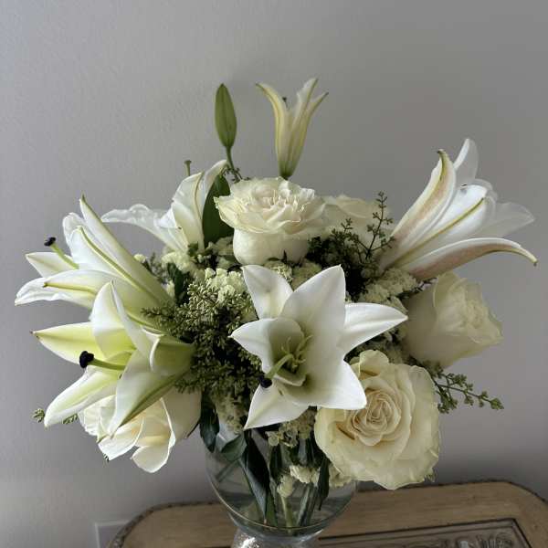 White lilies and roses arranged in a clear glass vase