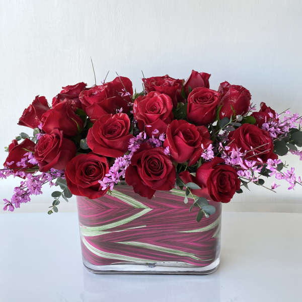 Red roses with pink filler flowers in a square glass vase