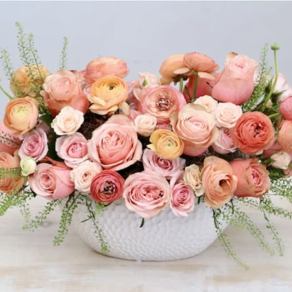 Low arrangement of peach and pink roses and ranunculus in a white ceramic bowl