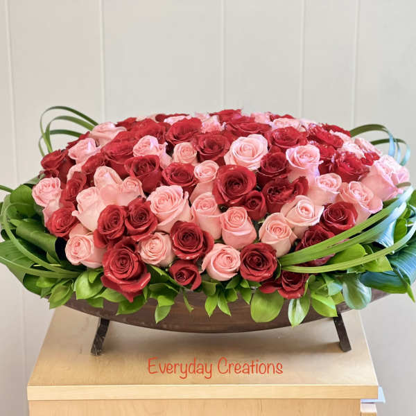 Oval arrangement of red and pink roses in a low wooden container