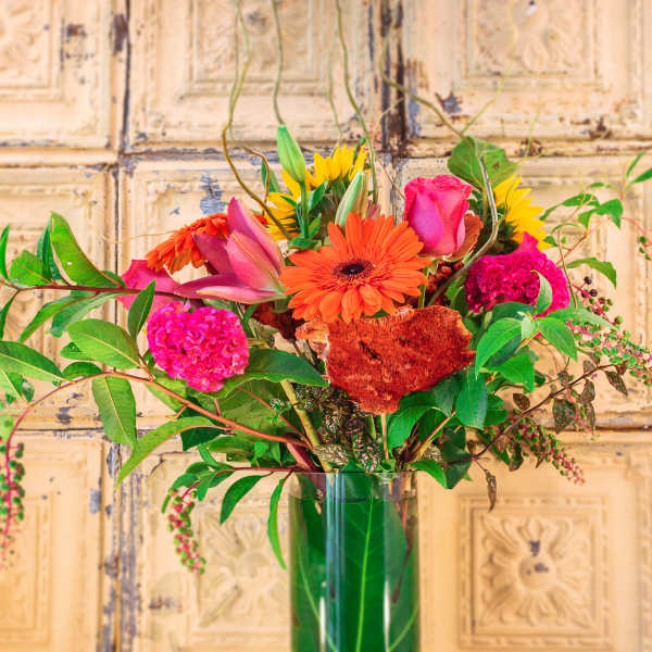 Bright mixed bouquet in a tall glass vase with pink, orange, and yellow blooms