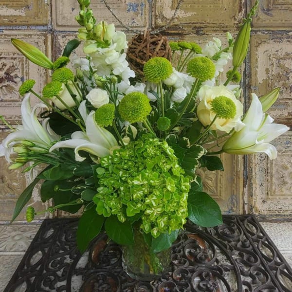 White lilies and green blooms arranged in a glass vase