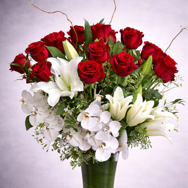 Red roses and white lilies with orchids in a tall green vase