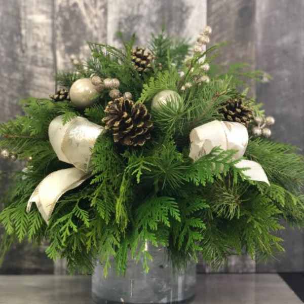 Evergreen arrangement with pinecones, cream ornaments, and ribbon in a glass vase