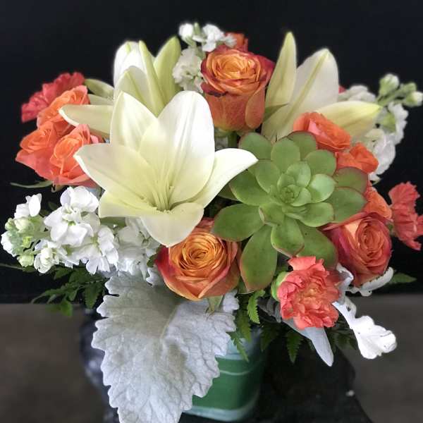 Bouquet of orange roses, white lilies, and a green succulent in a vase
