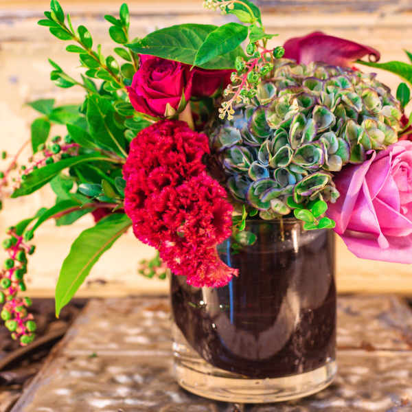 Mixed bouquet in a dark glass vase with pink roses and red blooms