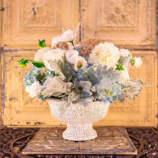White and pale blue floral arrangement in a decorative pedestal vase