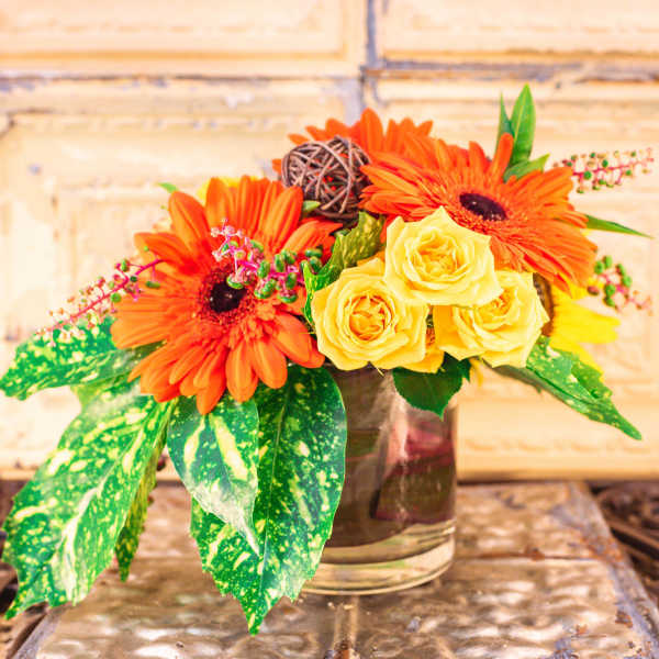 Orange gerbera daisies and yellow roses in a glass vase
