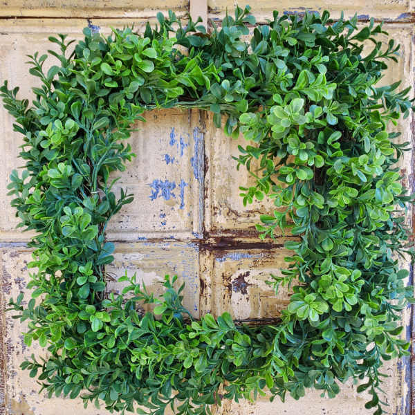 Square greenery wreath with dense green leaves on a rustic background