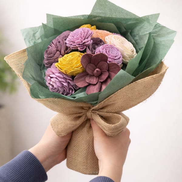 Handheld bouquet of multicolored flowers wrapped in burlap and green paper