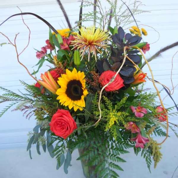 Tall mixed bouquet with sunflowers, red roses, and pink alstroemeria in a glass vase