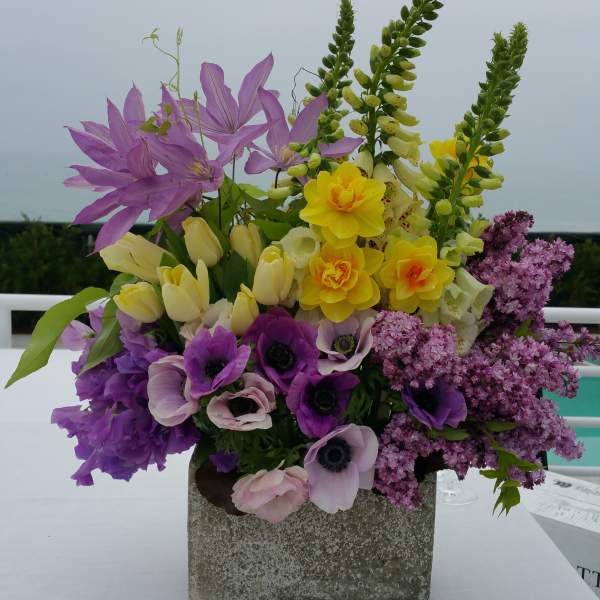 Mixed purple, yellow, and pink flowers arranged in a square stone vase