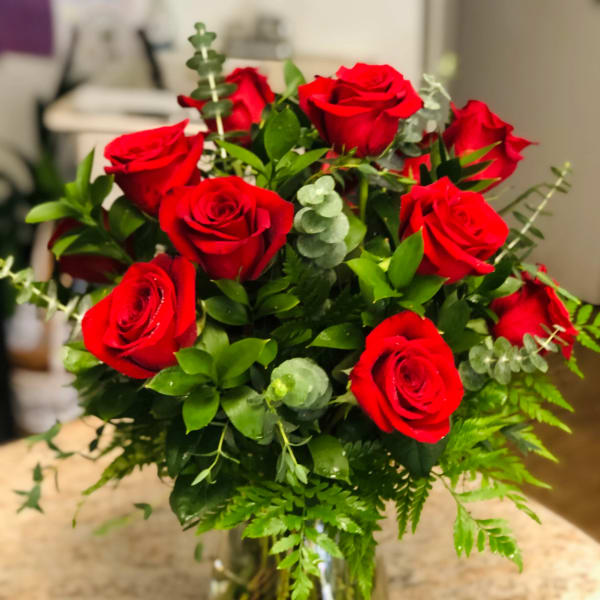 Red roses arranged in a clear glass vase with greenery