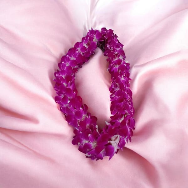 Purple orchid flower lei arranged in an oval shape on soft pink fabric