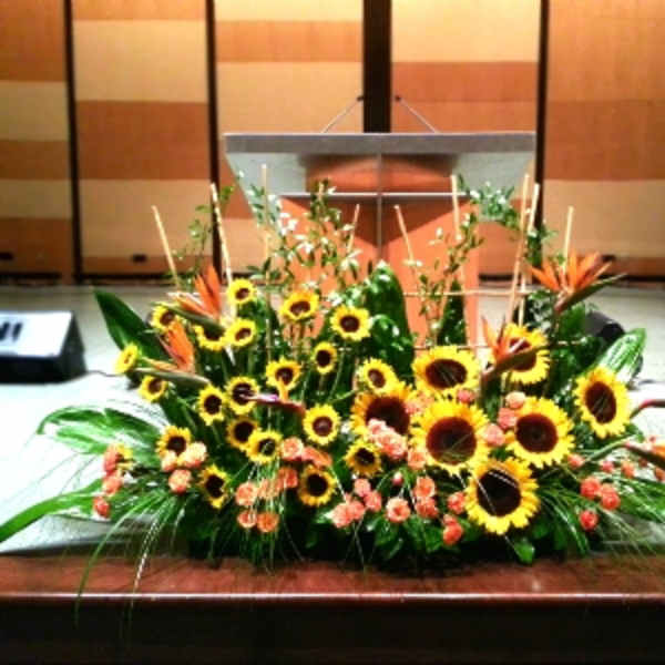 Large stage arrangement of yellow sunflowers and orange blooms in a low spray in front of a podium