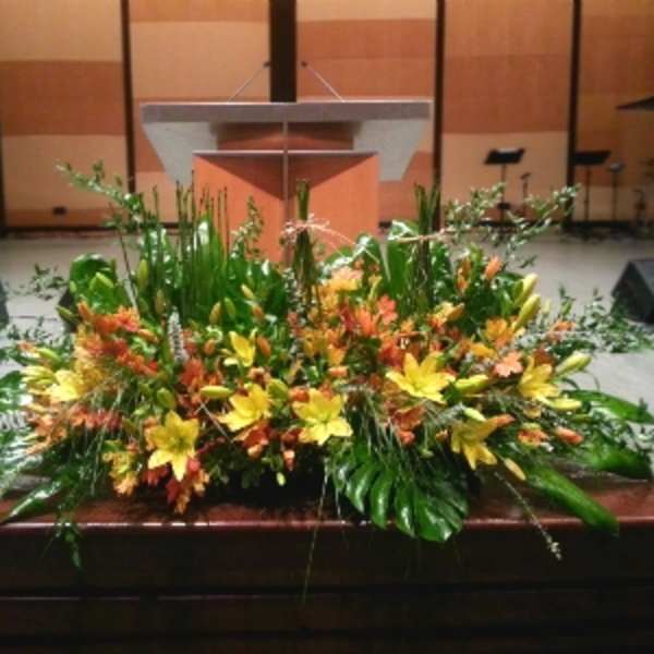 Large yellow and orange floral arrangement with lilies in front of a wooden podium