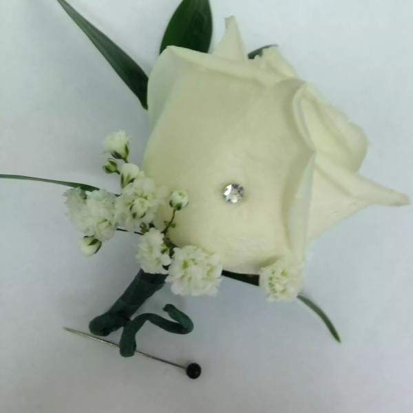 White rose boutonniere with small white blossoms and green leaves