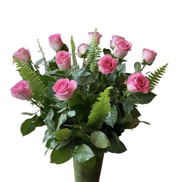 Pink roses arranged in a tall glass vase with fern foliage