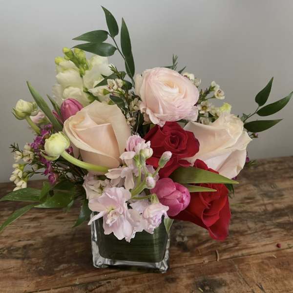 Mixed bouquet of roses, ranunculus, and snapdragons in a square glass vase