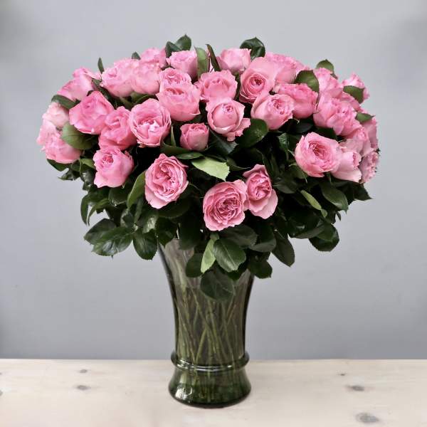 Large arrangement of pink roses in a tall clear glass vase against a gray background