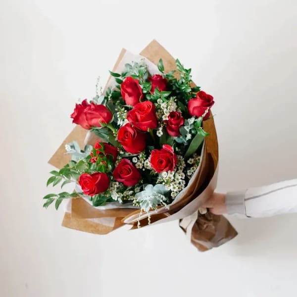 Handheld bouquet of red roses wrapped in brown paper