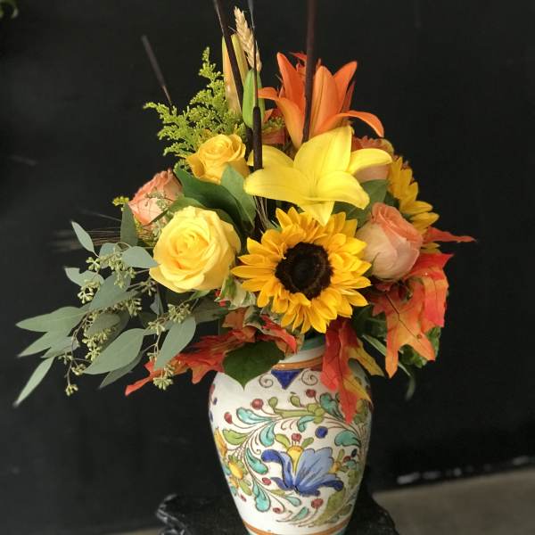Colorful bouquet of roses, lilies, and a sunflower in a painted vase