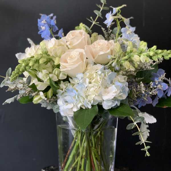 Bouquet of pale roses, hydrangeas, and blue flowers in a clear glass vase