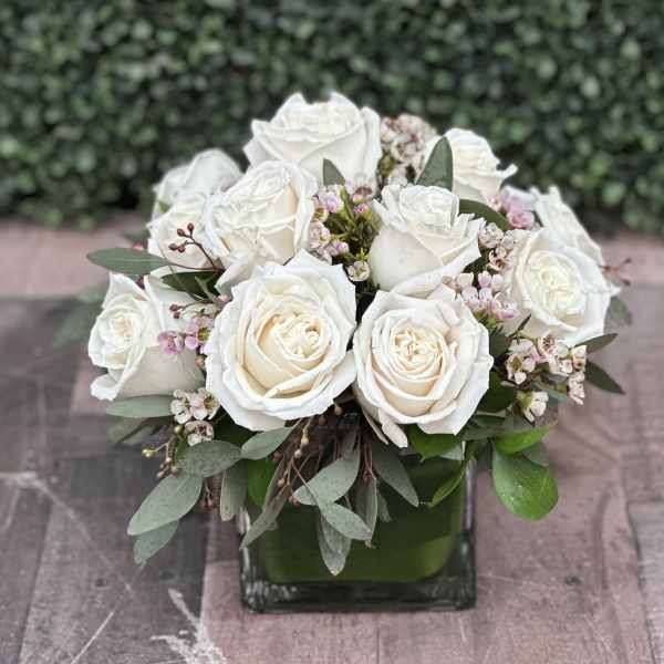 White rose bouquet in a square glass vase with small pink blossoms
