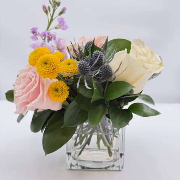 Pink and white roses with yellow blooms in a clear glass vase